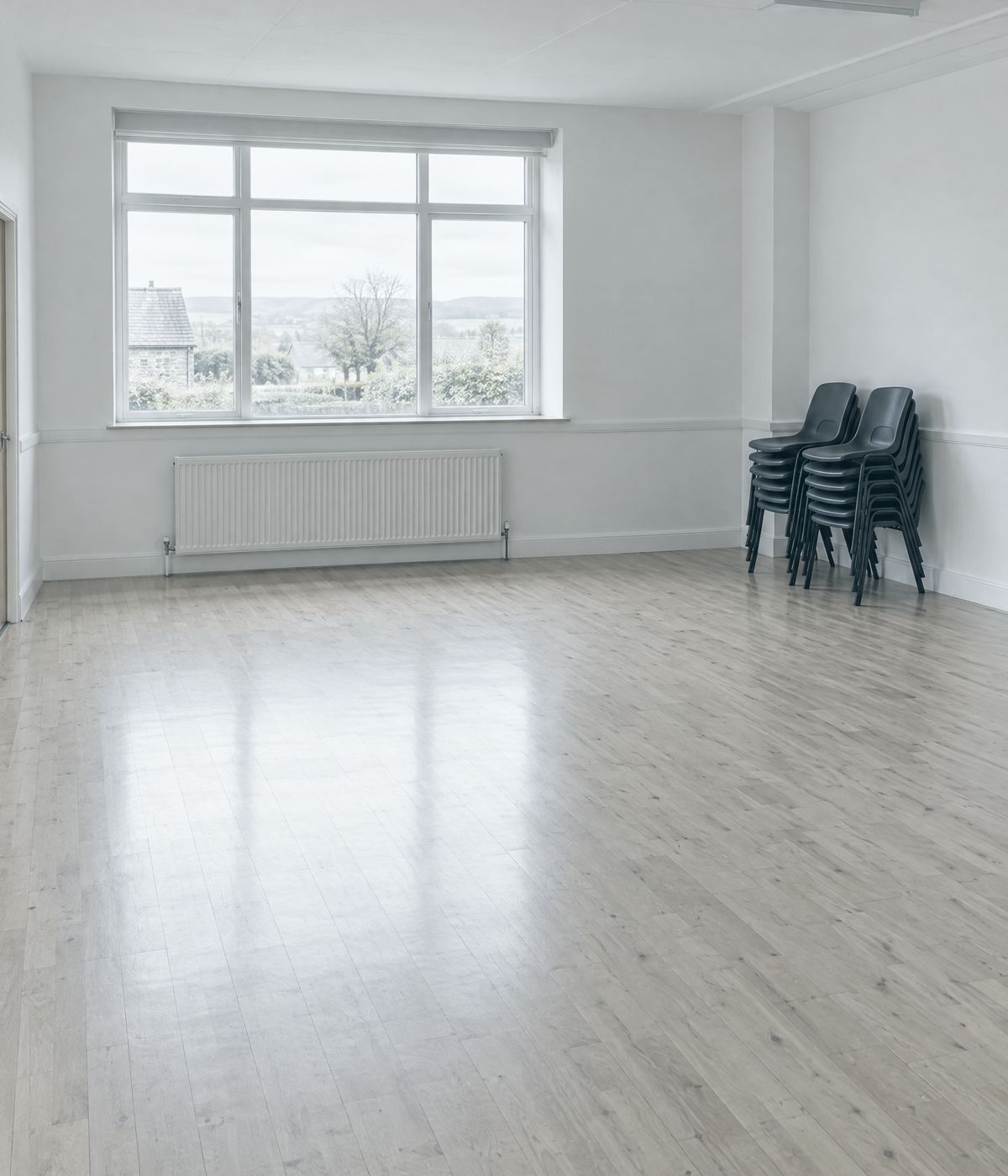Sala diáfana de un centro cultural, con suelo de madera y sillas apiladas a un lado