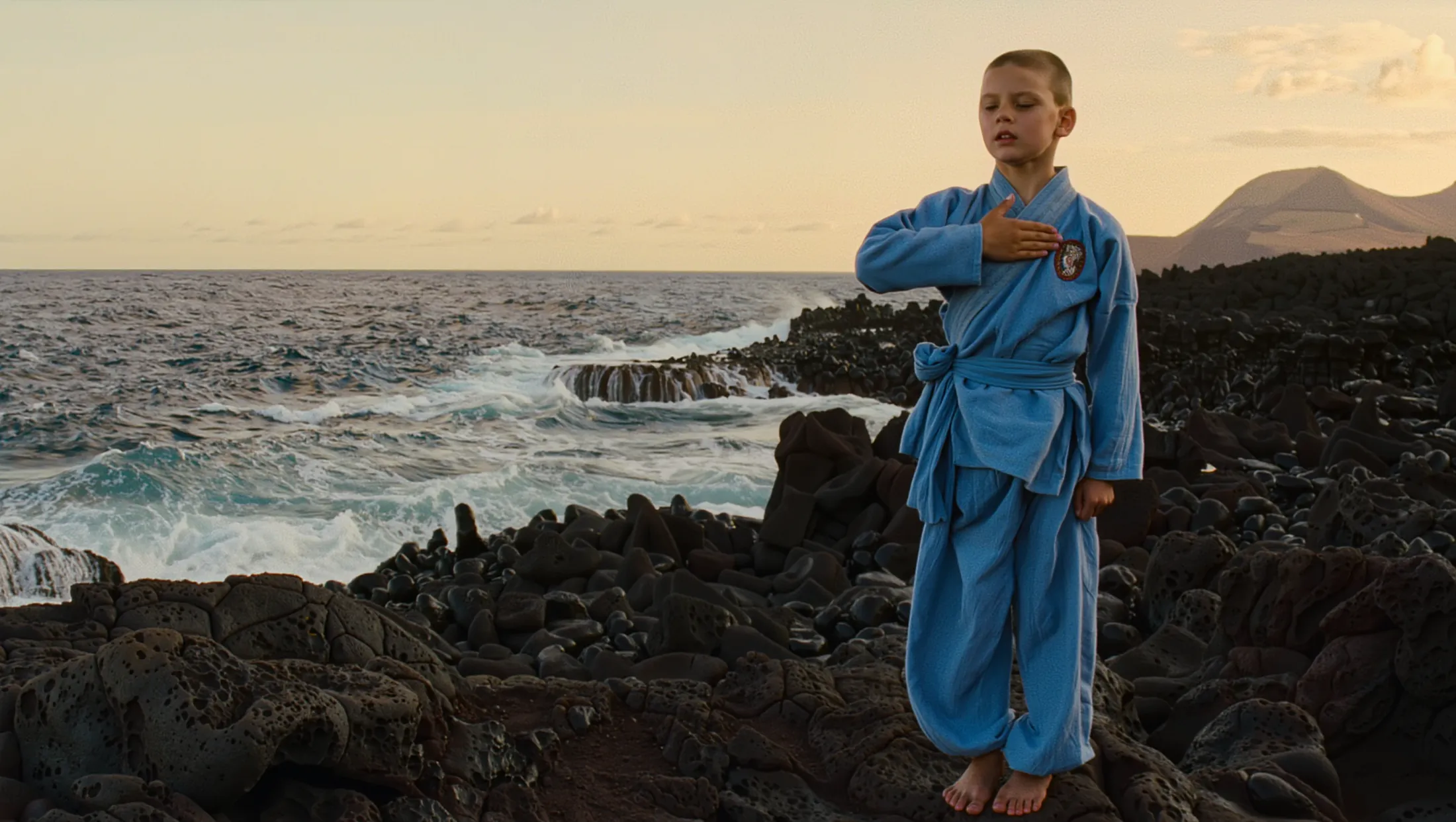 Vovinam student in the sky-blue uniform performing the salute facing the sea at dawn, on the lava coastline of Garachico with Mount Teide behind